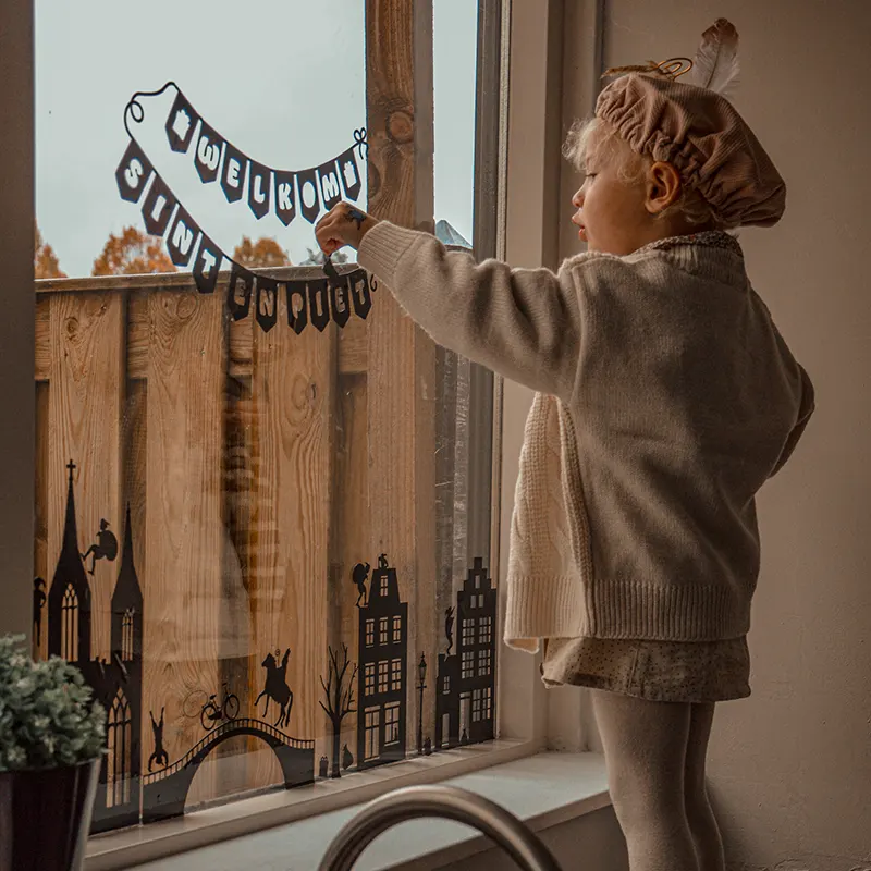 raamstickers sinterklaas huisjes geplakt op het raam door een meisje verkleed als een pietje