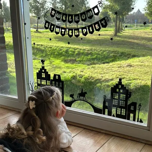statische raamstickers huisjes voor sinterklaas geplakt op het raam en een meisje kijkt erna