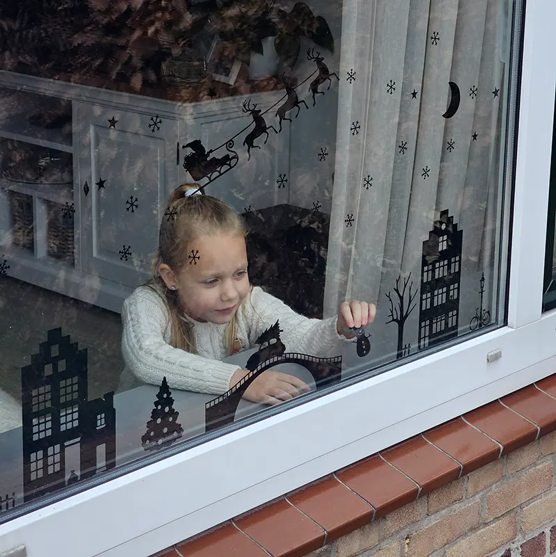 raamstickers voor sinterklaas en kerst geplakt op het raam door een meisje