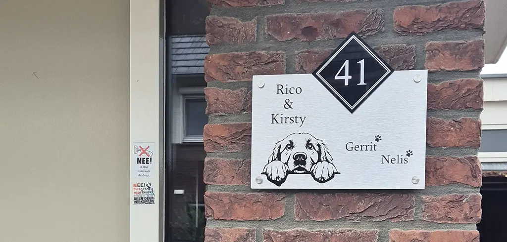 Stickers - Kiedoka 2 RVS naambordje met een glurende hond erop die hangt aan de muur bij de voordeur